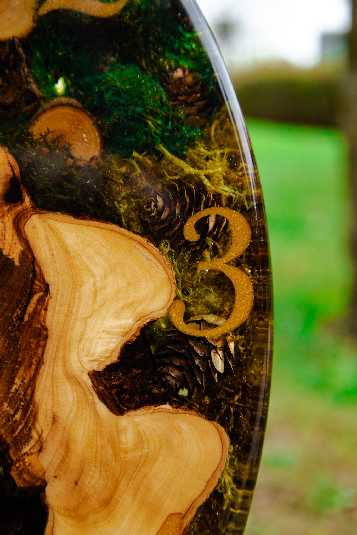 Forest Whisper - Handgefertigte Wanduhr aus Olivenholz mit Moos, kleinen Zapfen und Epoxidharz.