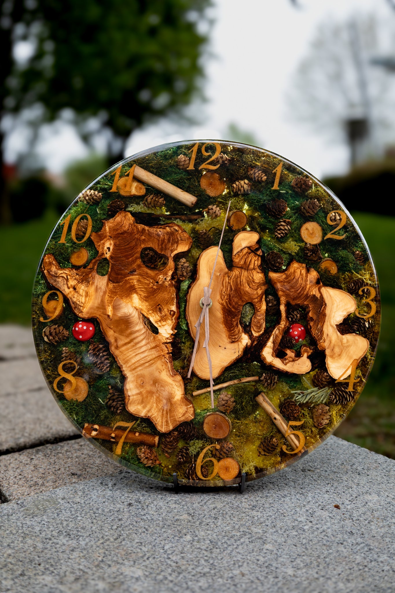 Forest Whisper - Handgefertigte Wanduhr aus Olivenholz mit Moos, kleinen Zapfen und Epoxidharz.